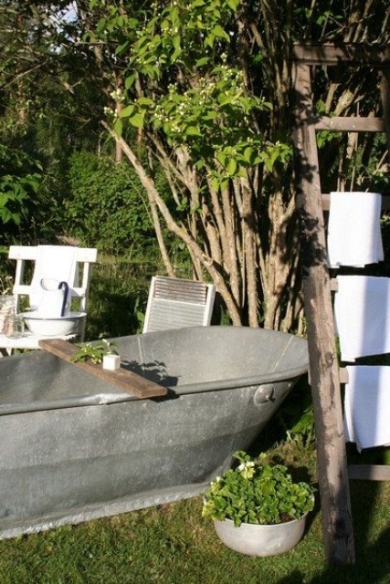 un bagno esterno rustico con vasca in metallo, vegetazione in vaso e alberi viventi