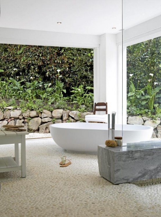 un moderno bagno esterno con vasca ovale, panca in marmo e tavoli in legno