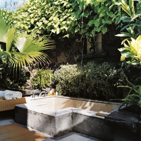 un raffinato bagno esterno con vasca in cemento, panca con asciugamani e verde