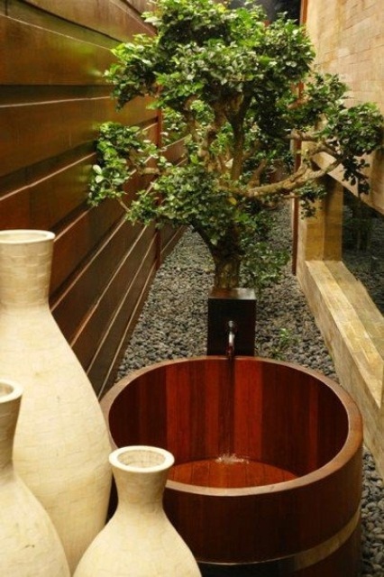 un bagno giapponese all'aperto con una vasca da bagno in legno, un albero piantato e vasi
