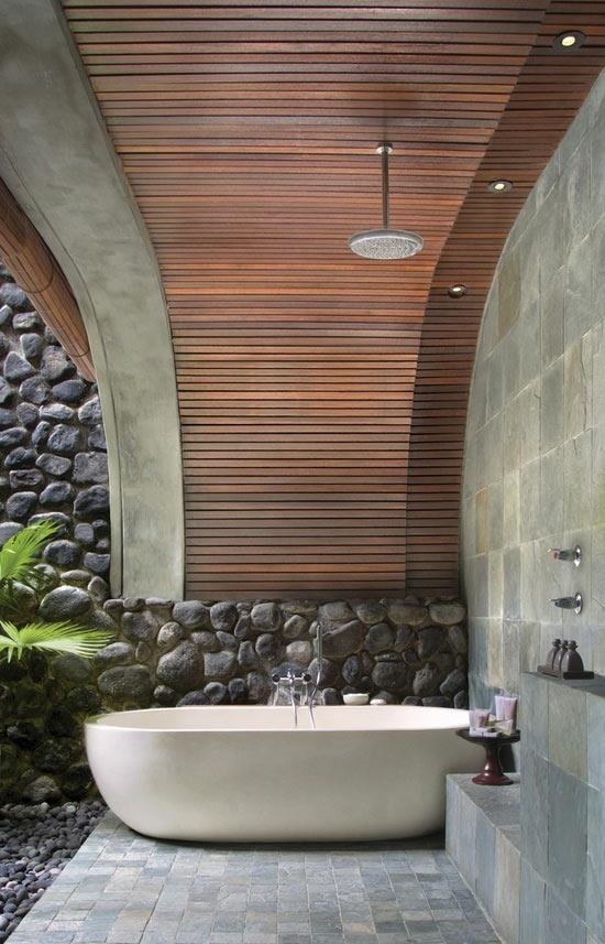un moderno bagno esterno con vasca ovale, piastrelle e un muro di pietra