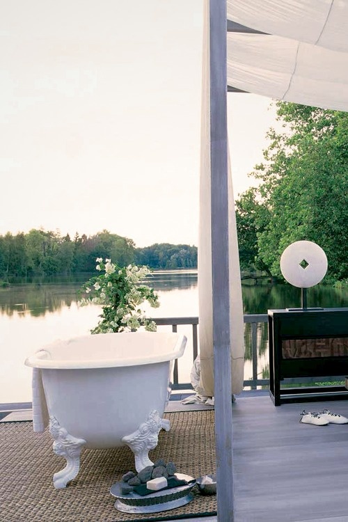 un raffinato bagno esterno con vasca bianca, fiori in vaso e un tappeto per l'intimità