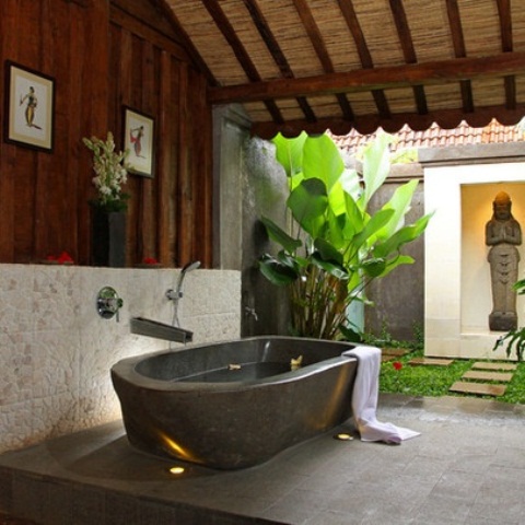 un bagno esterno di ispirazione zen con tanto verde, una vasca in pietra e una statua