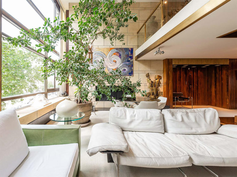 Il soggiorno è arredato con mobili bianchi, una grande pianta in vaso e alcune opere d'arte colorate