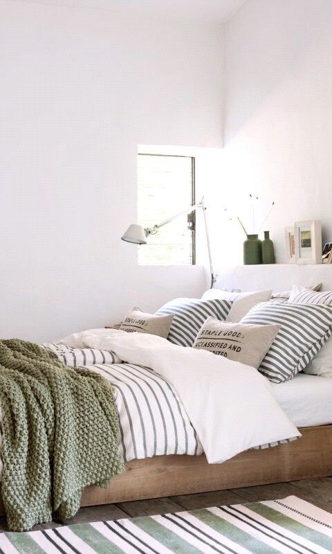 strisce, stampe industriali sui cuscini e una coperta verde all'uncinetto creano un letto fresco e pronto per la primavera
