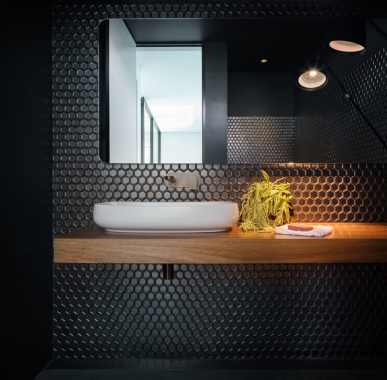 Il bagno è realizzato con piastrelle esagonali nere e una vanità fluttuante