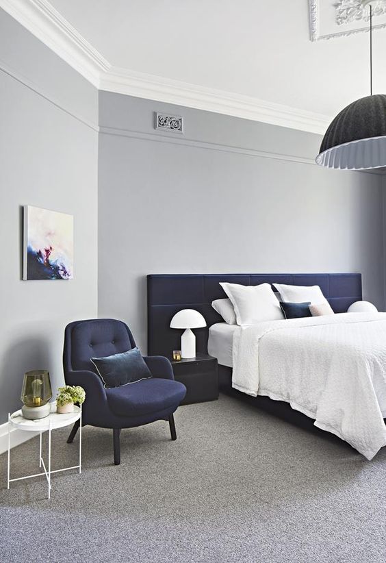 una camera da letto ariosa in grigio chiaro con un letto e una sedia imbottiti blu scuro per un look audace