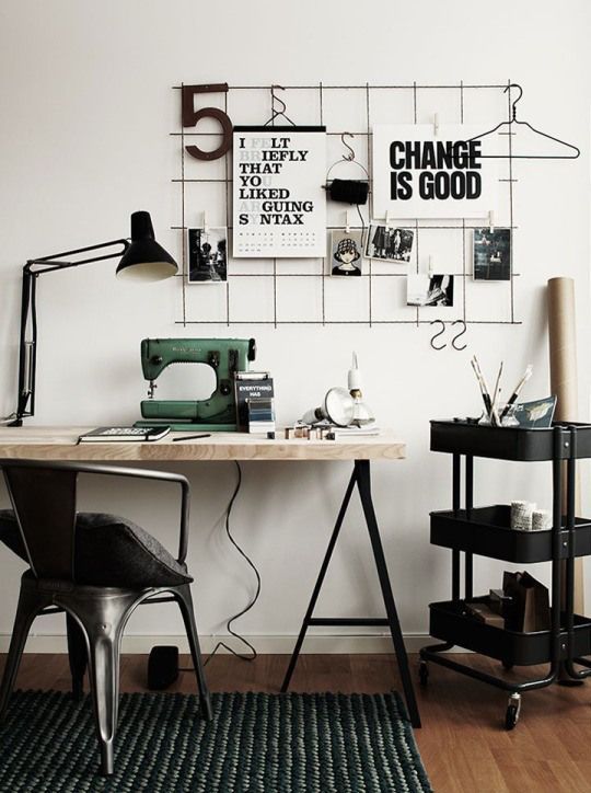 un ufficio in casa scandinavo in bianco e nero con una griglia con note, una scrivania su cavalletto, un carrello IKEA Raskog e lampade