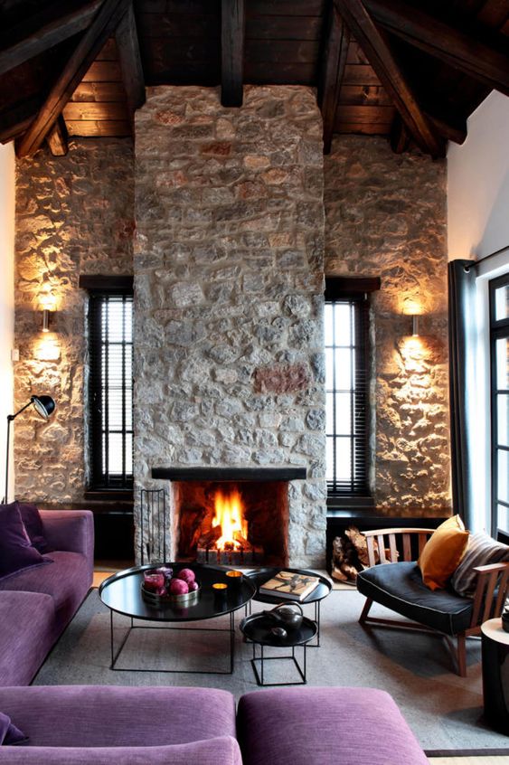 un luminoso soggiorno contemporaneo con pareti in pietra grezza e camino, mobili viola ed eleganti tavoli rotondi