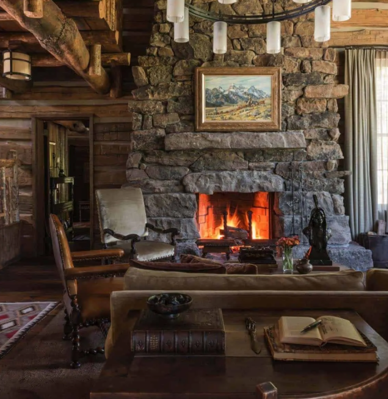 un soggiorno in stile cabina fatto con molto legno grezzo, un grande focolare in pietra e mobili vintage in legno e pelle