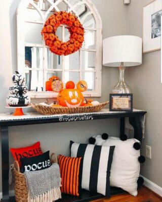una luminosa console d'ingresso di Halloween con cuscini neri, bianchi e arancioni, una zucca di Halloween, una ghirlanda di zucca e una pila di zucche bianche