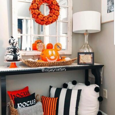 una luminosa console d'ingresso di Halloween con cuscini neri, bianchi e arancioni, una zucca di Halloween, una ghirlanda di zucca e una pila di zucche bianche