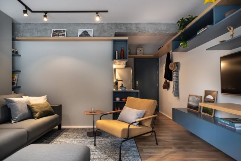 Il soggiorno è fatto in blu e grigio, con mobili imbottiti e in pelle, con luci e uno spazio per l'home office